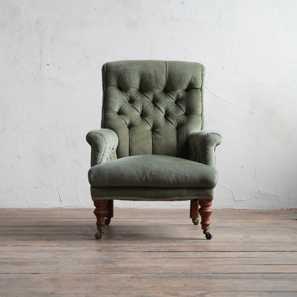 An antique green velvet armchair with button tufting, turned wooden legs, and brass castors. View II