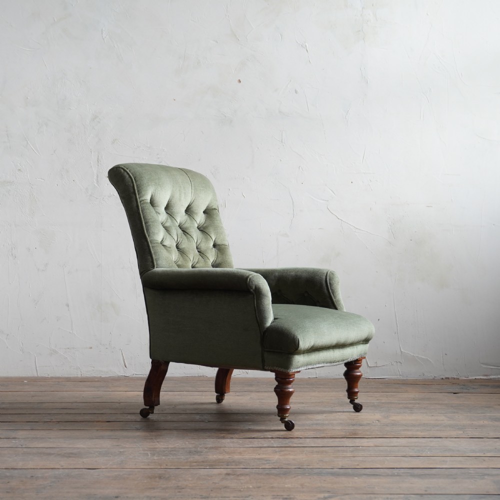 An antique green velvet armchair with button tufting, turned wooden legs, and brass castors. View III