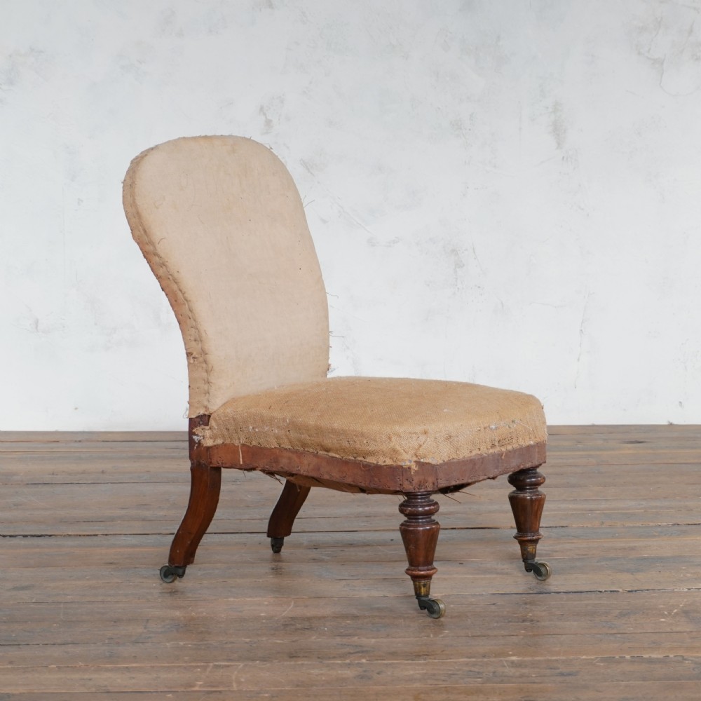 An antique Victorian bedroom chair with exposed hessian upholstery, wooden frame, and turned front legs with castors.