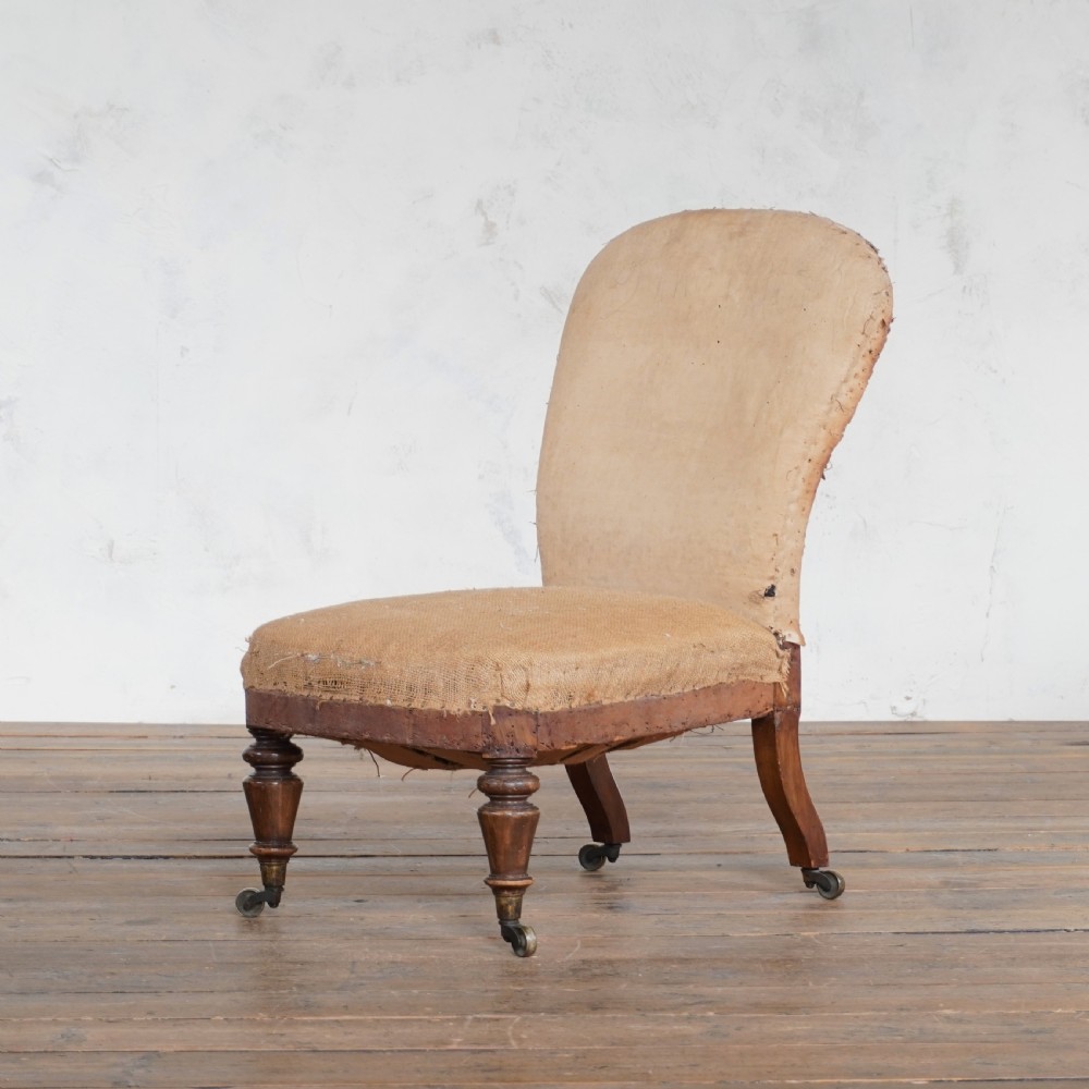 An antique Victorian bedroom chair with exposed hessian upholstery, wooden frame, and turned front legs with castors. View III