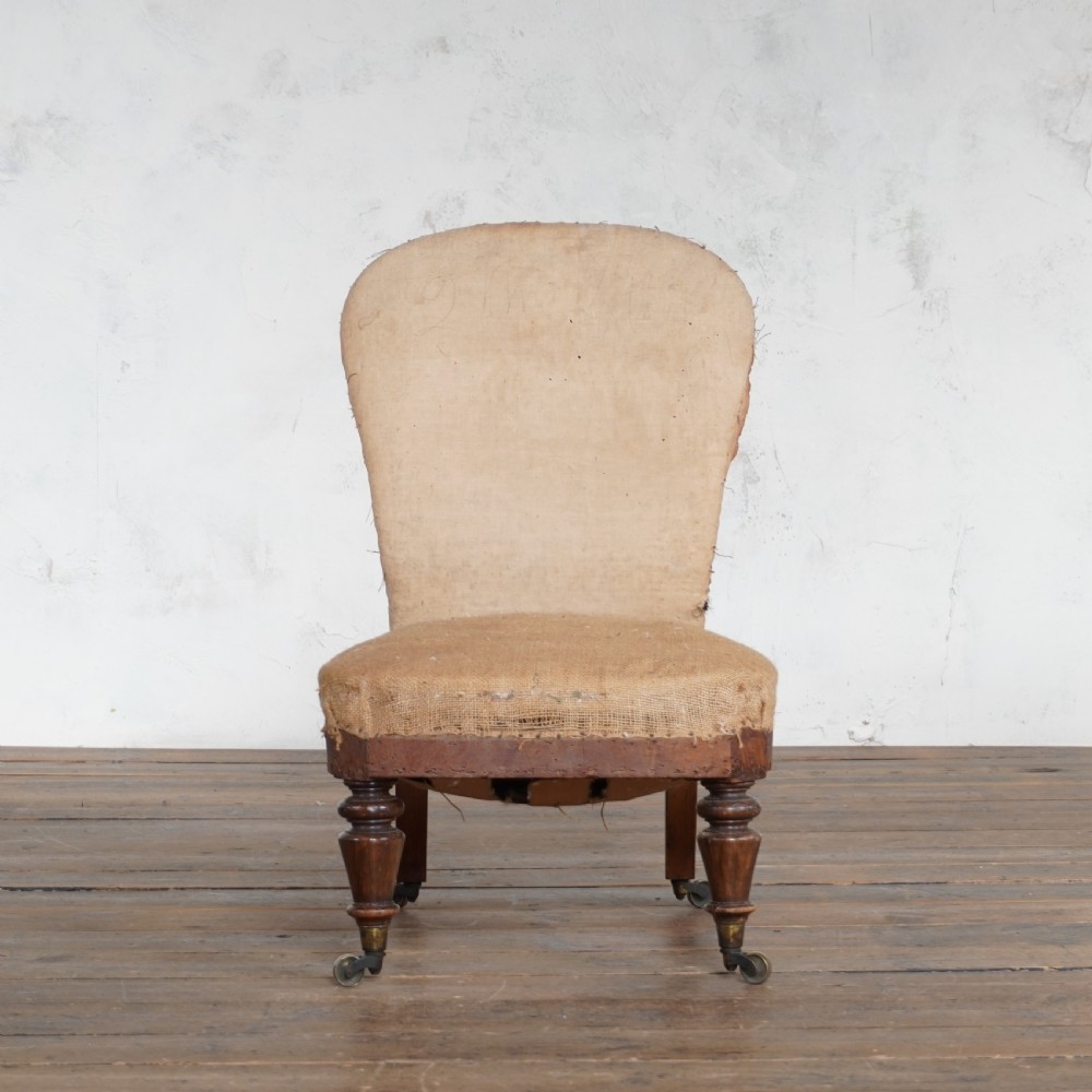 An antique Victorian bedroom chair with exposed hessian upholstery, wooden frame, and turned front legs with castors. View IV