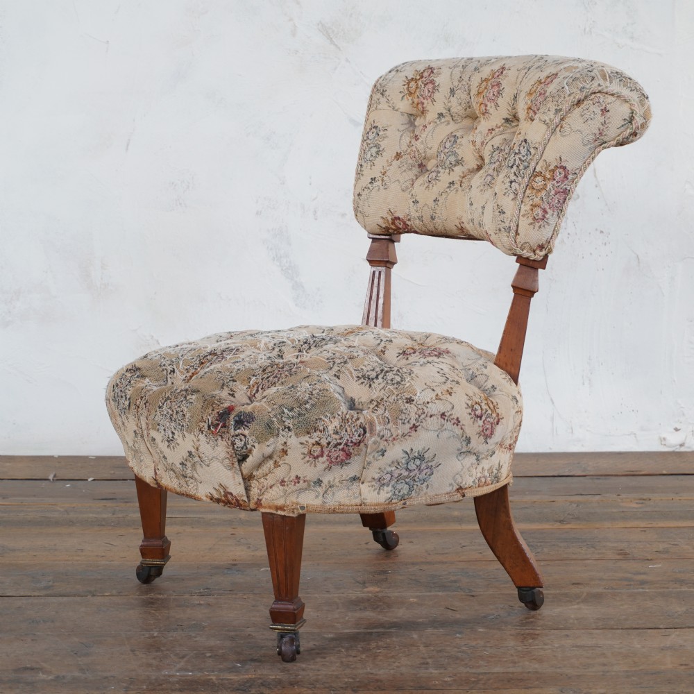 A Victorian low-seated slipper chair with deep-buttoned floral tapestry upholstery, supported by fluted front timber legs on brass castors.