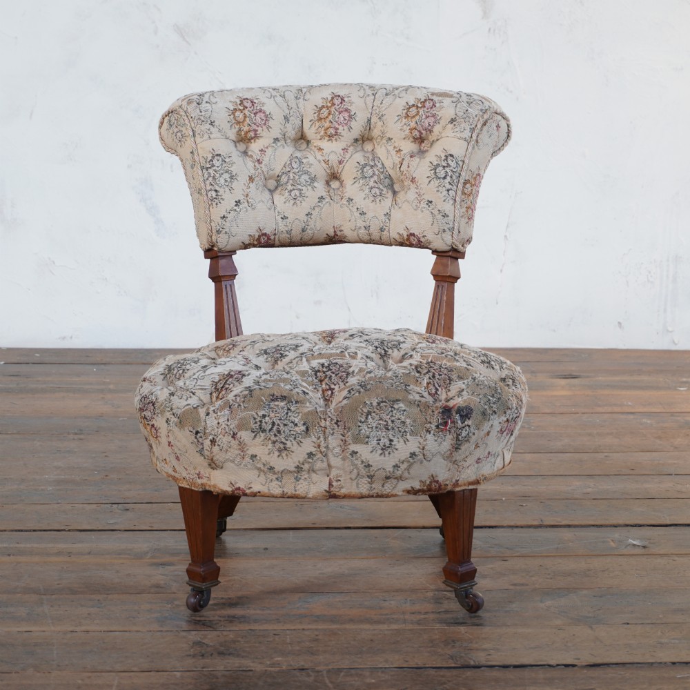 A Victorian low-seated slipper chair with deep-buttoned floral tapestry upholstery, supported by fluted front timber legs on brass castors. View V