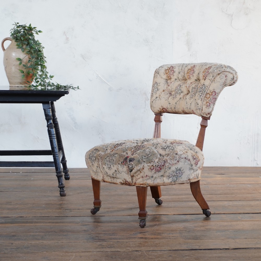 A Victorian low-seated slipper chair with deep-buttoned floral tapestry upholstery, supported by fluted front timber legs on brass castors. View VI