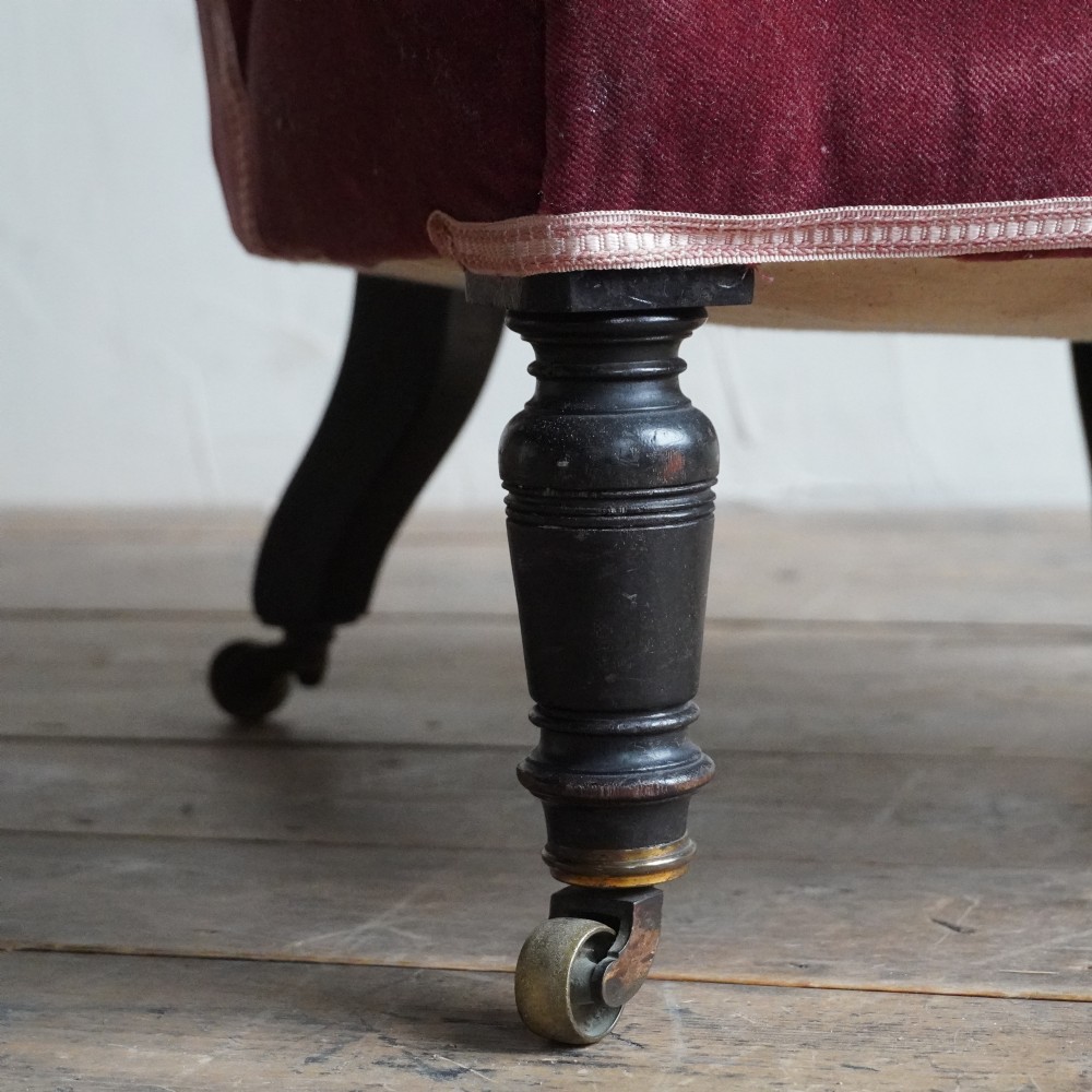 A low Victorian slipper chair upholstered in deep buttoned rose-pink velvet with turned dark front legs on brass castors. View VI