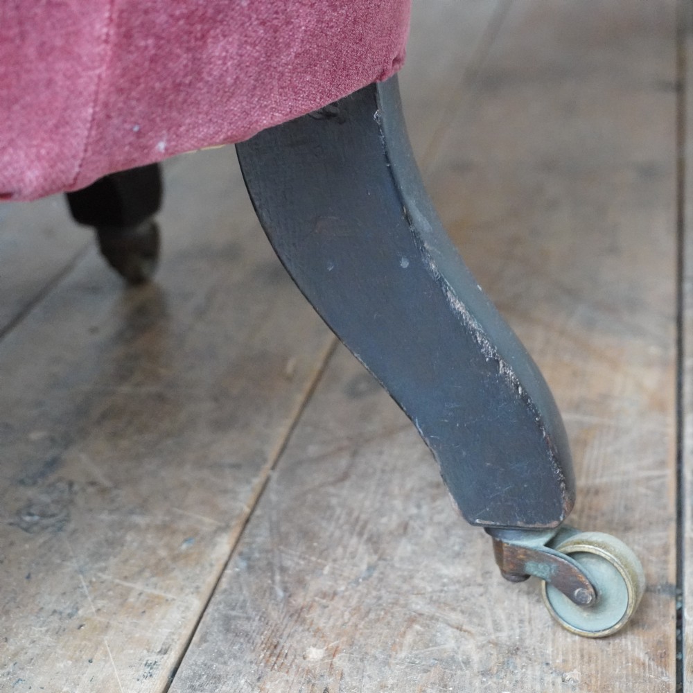 A low Victorian slipper chair upholstered in deep buttoned rose-pink velvet with turned dark front legs on brass castors. View VII