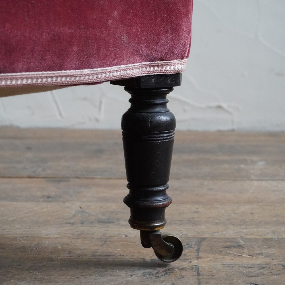 A low Victorian slipper chair upholstered in deep buttoned rose-pink velvet with turned dark front legs on brass castors. View VIII