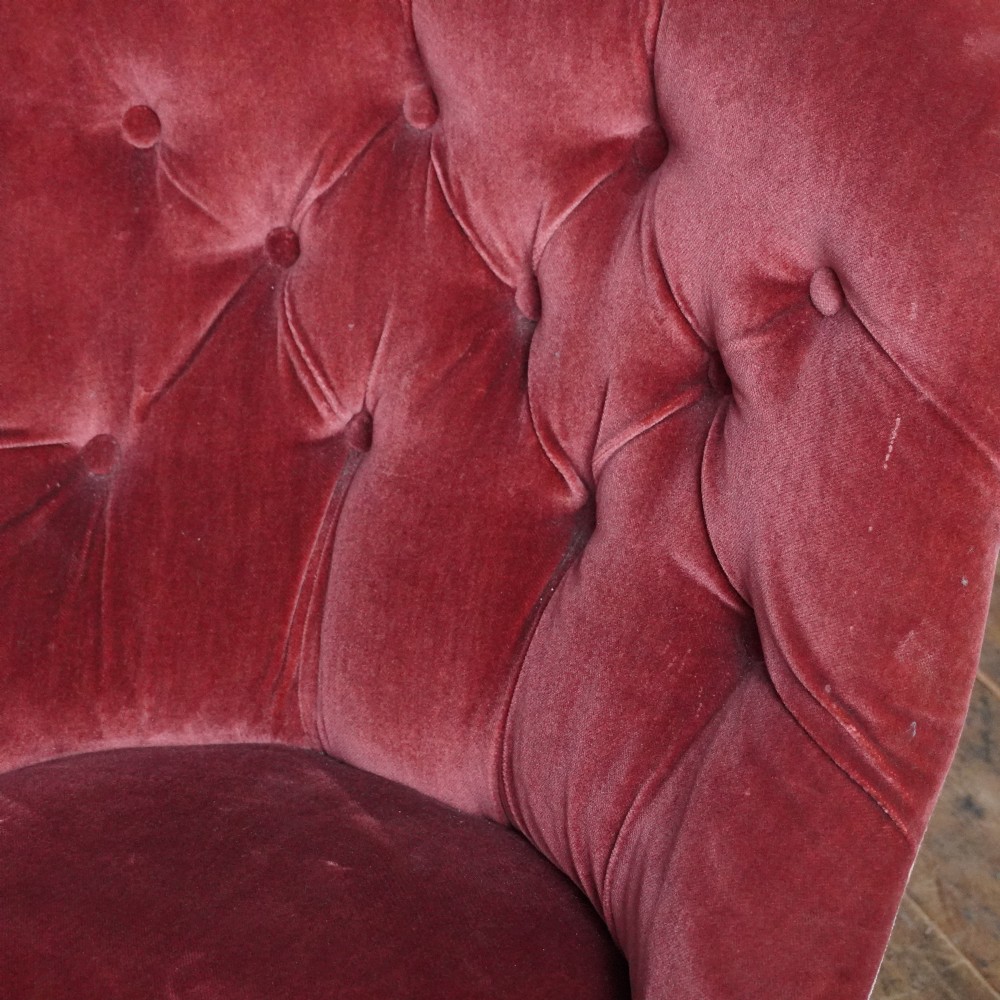 A low Victorian slipper chair upholstered in deep buttoned rose-pink velvet with turned dark front legs on brass castors. View IX
