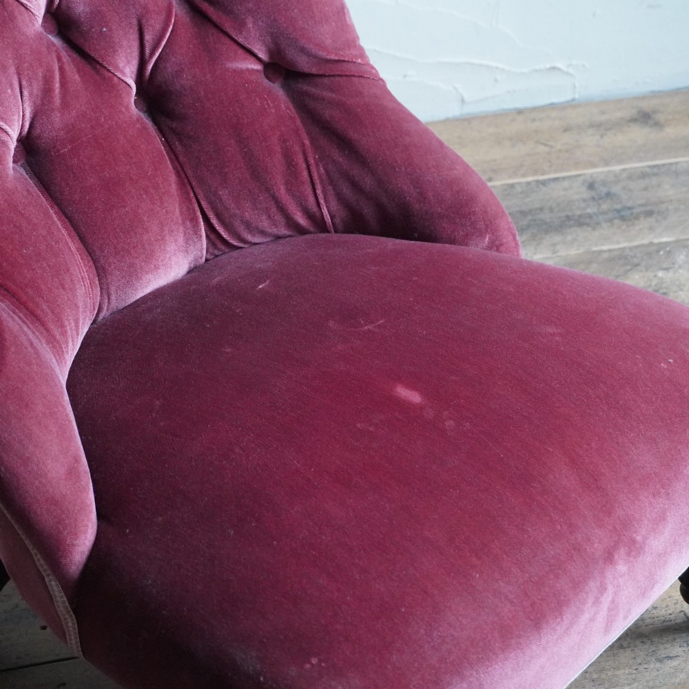 A low Victorian slipper chair upholstered in deep buttoned rose-pink velvet with turned dark front legs on brass castors. View X