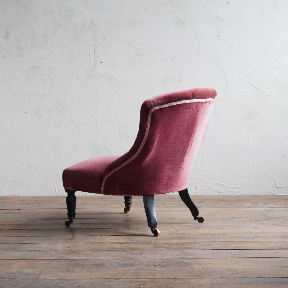 A low Victorian slipper chair upholstered in deep buttoned rose-pink velvet with turned dark front legs on brass castors. View XI