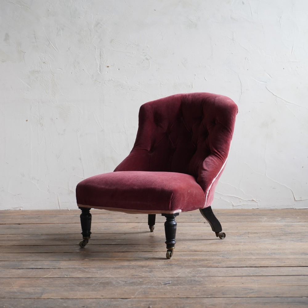 A low Victorian slipper chair upholstered in deep buttoned rose-pink velvet with turned dark front legs on brass castors. View XII