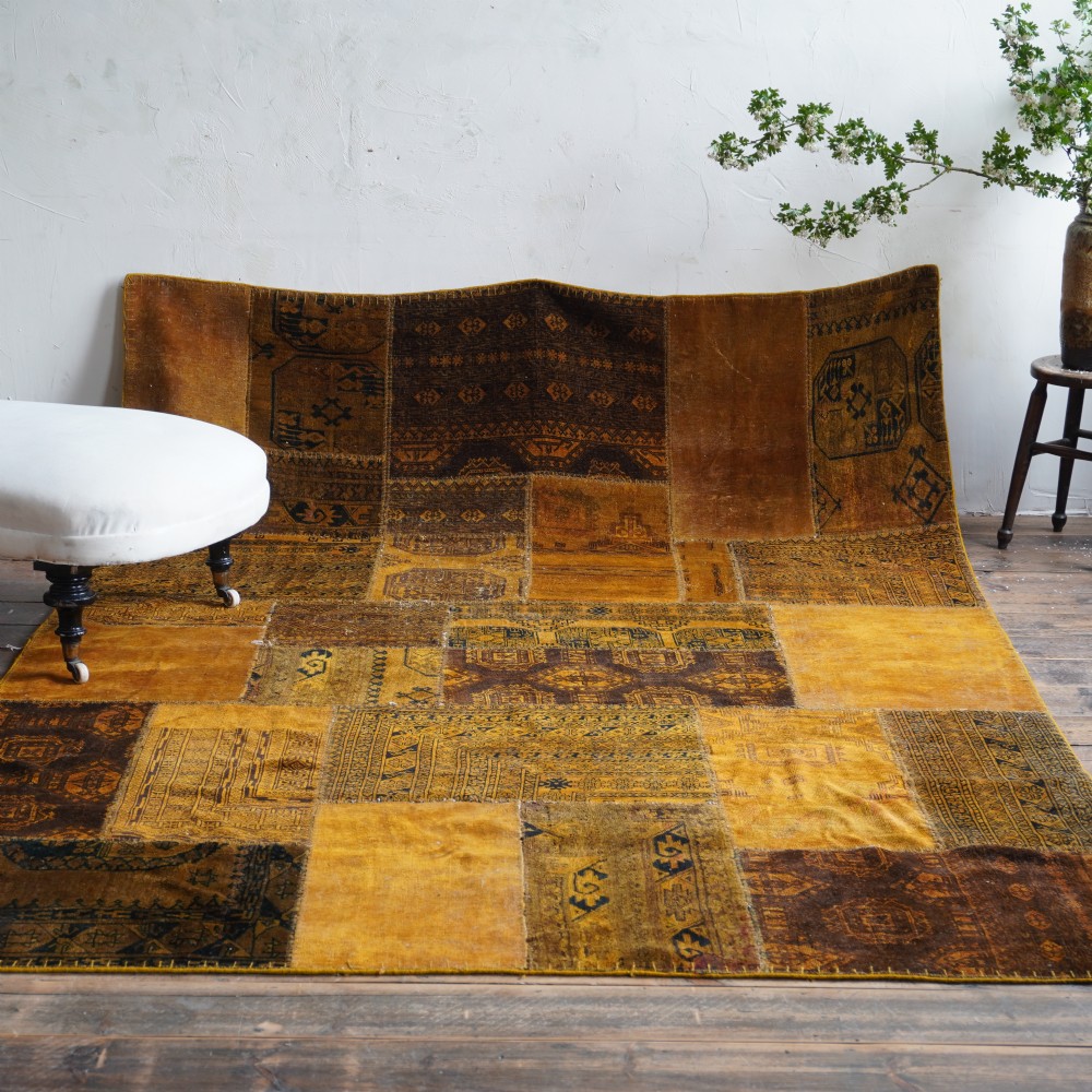 An antique patchwork rug composed of various geometric and patterned wool fragments in shades of brown and ochre.