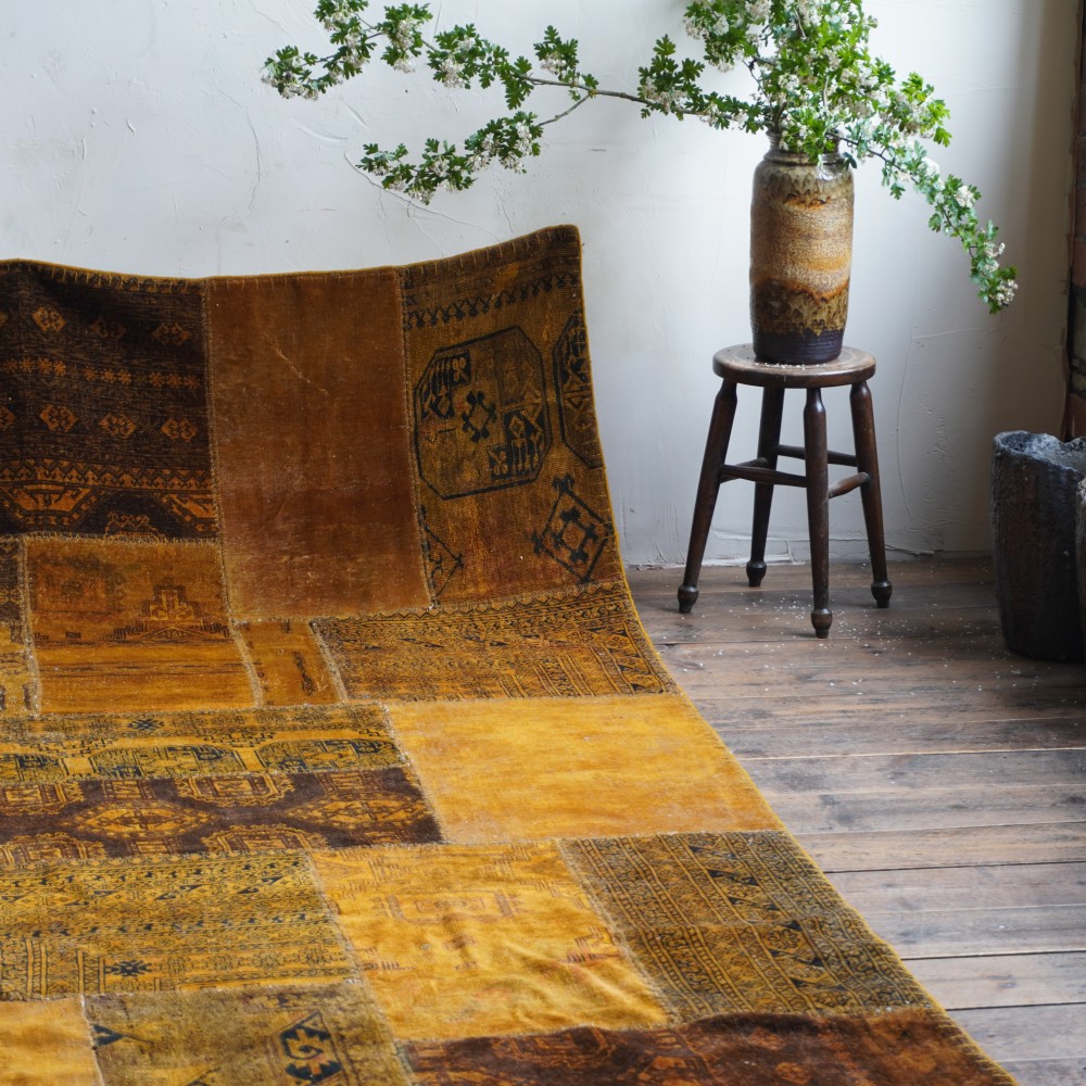 An antique patchwork rug composed of various geometric and patterned wool fragments in shades of brown and ochre. View II