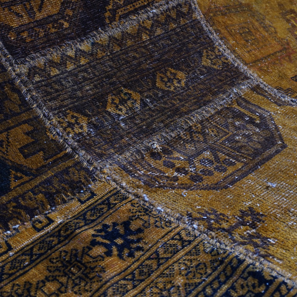 An antique patchwork rug composed of various geometric and patterned wool fragments in shades of brown and ochre. View III
