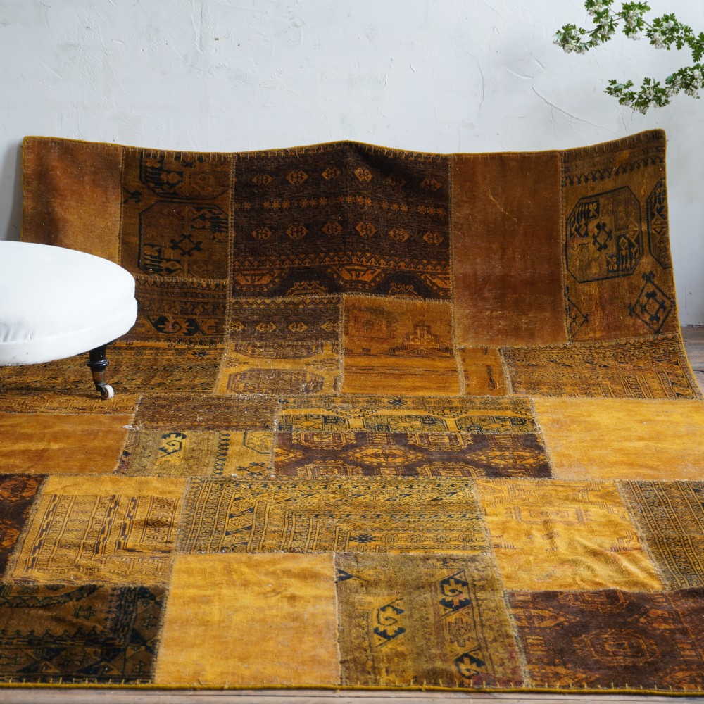 An antique patchwork rug composed of various geometric and patterned wool fragments in shades of brown and ochre. View IV