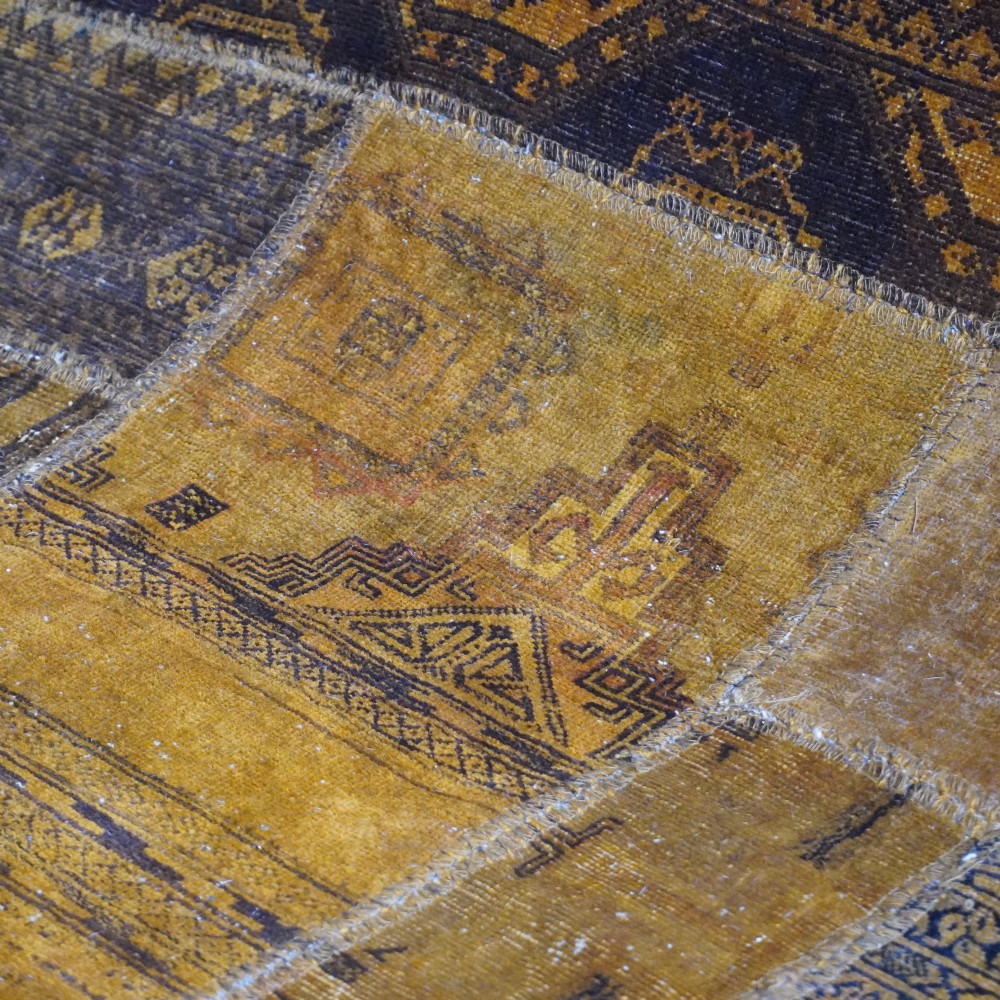 An antique patchwork rug composed of various geometric and patterned wool fragments in shades of brown and ochre. View V