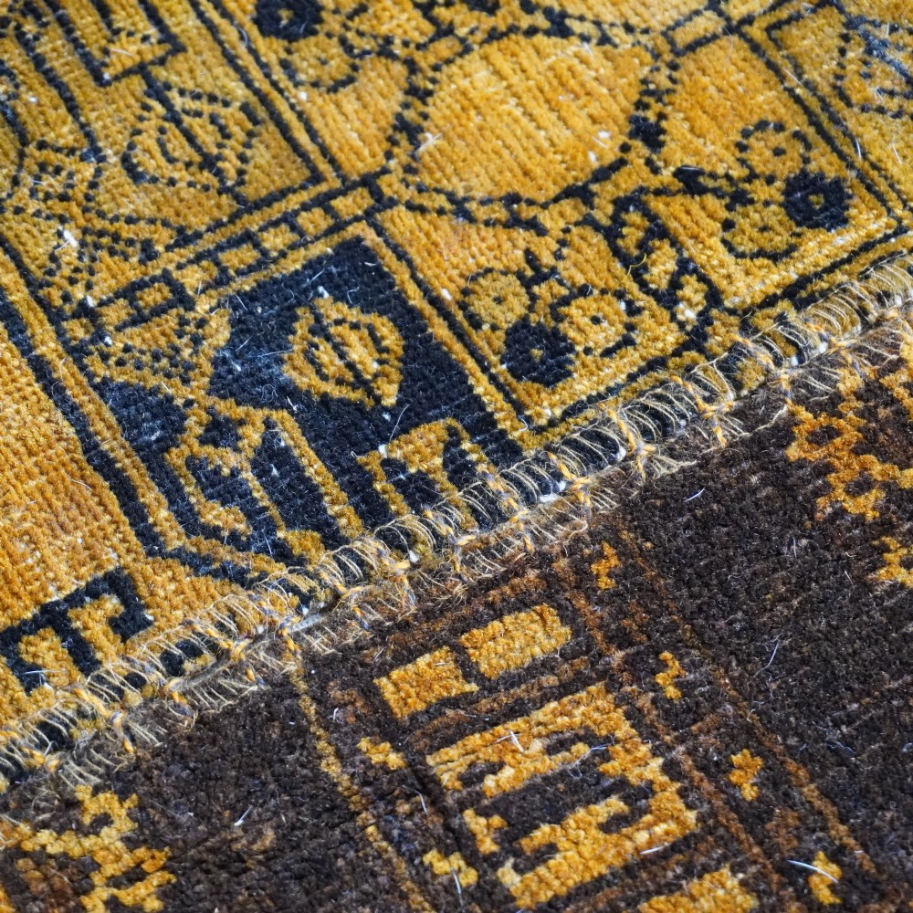 An antique patchwork rug composed of various geometric and patterned wool fragments in shades of brown and ochre. View VI