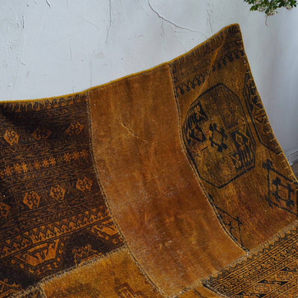 An antique patchwork rug composed of various geometric and patterned wool fragments in shades of brown and ochre. View VII