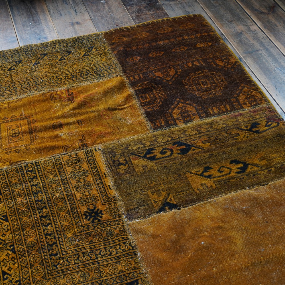 An antique patchwork rug composed of various geometric and patterned wool fragments in shades of brown and ochre. View VIII