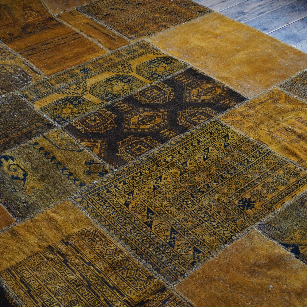 An antique patchwork rug composed of various geometric and patterned wool fragments in shades of brown and ochre. View IX