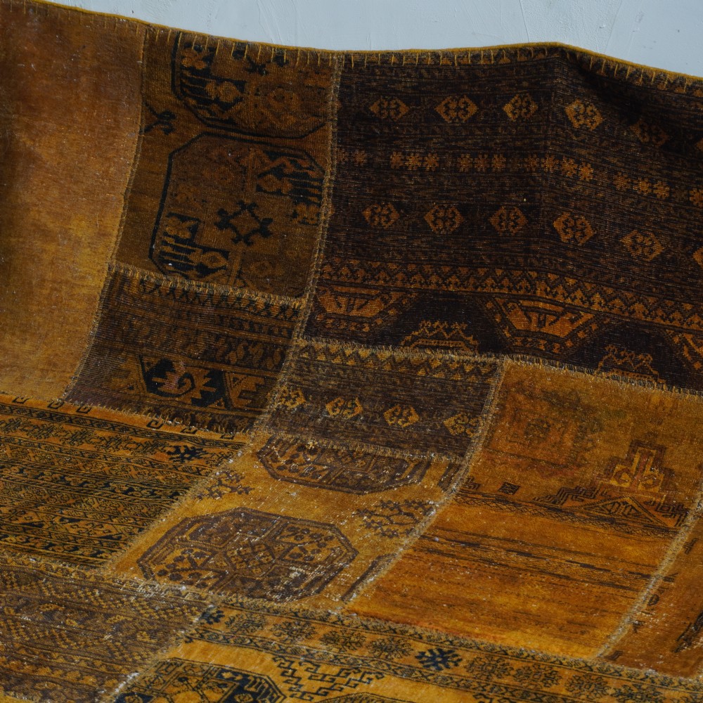 An antique patchwork rug composed of various geometric and patterned wool fragments in shades of brown and ochre. View X