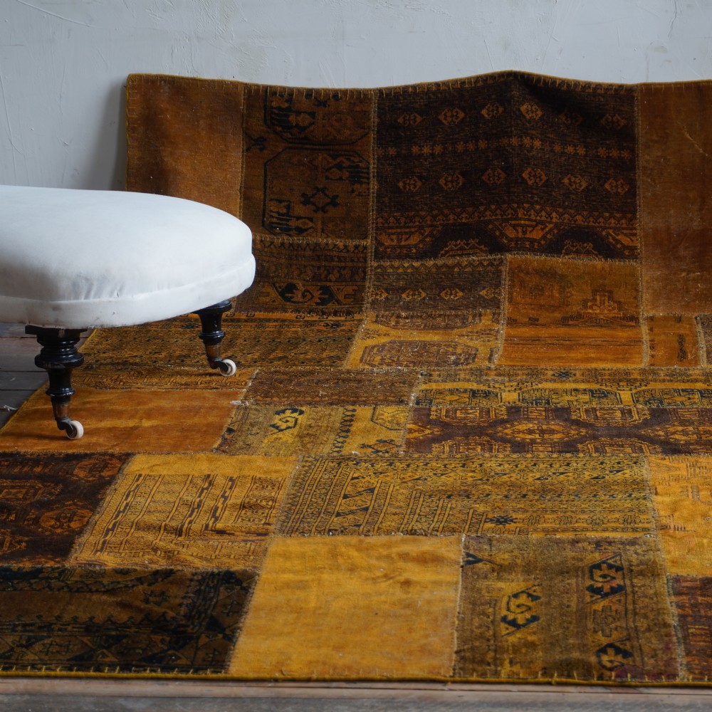 An antique patchwork rug composed of various geometric and patterned wool fragments in shades of brown and ochre. View XI
