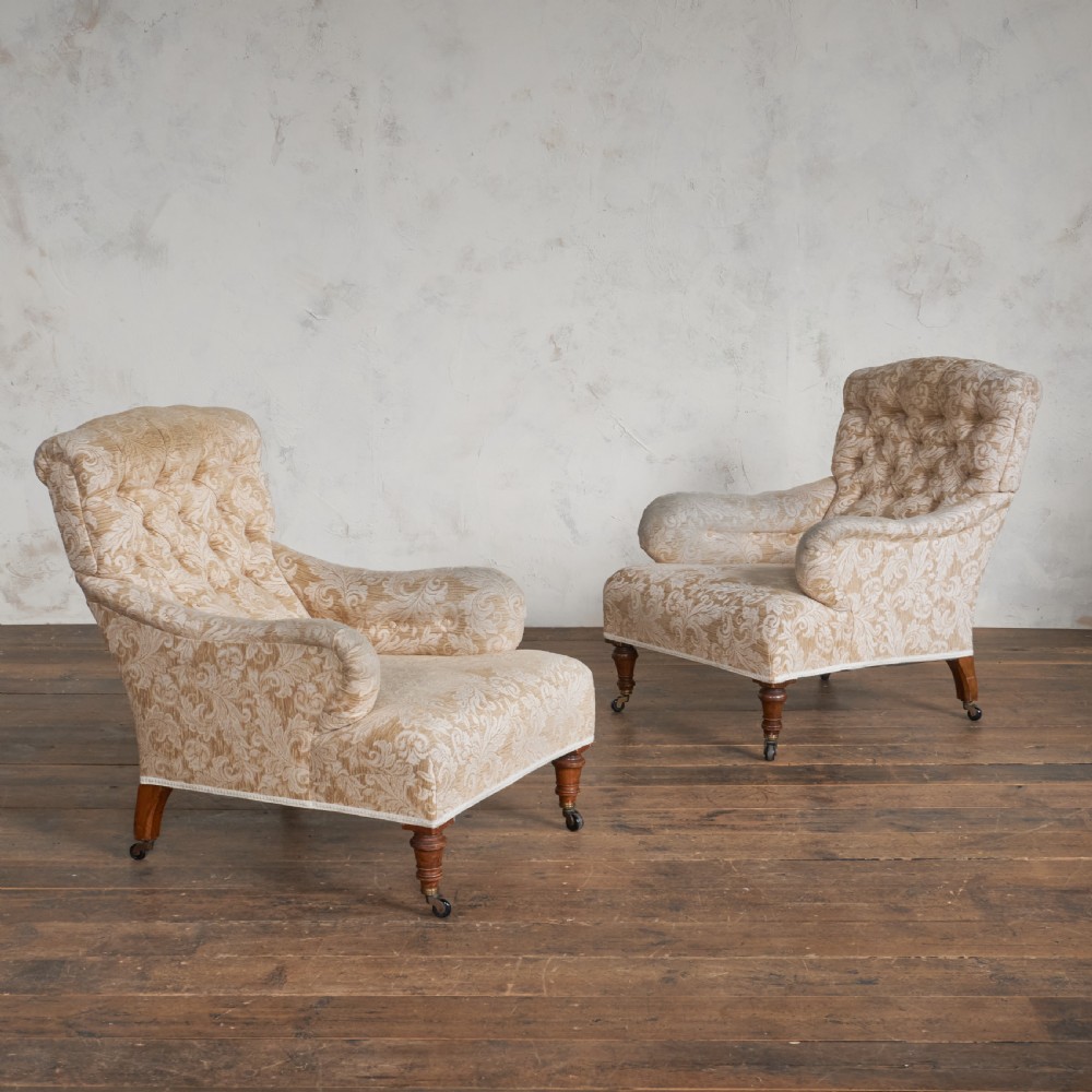 A pair of Victorian Howard style armchairs upholstered in a patterned beige fabric, featuring buttoned backs and turned wooden legs with brass castors. View II