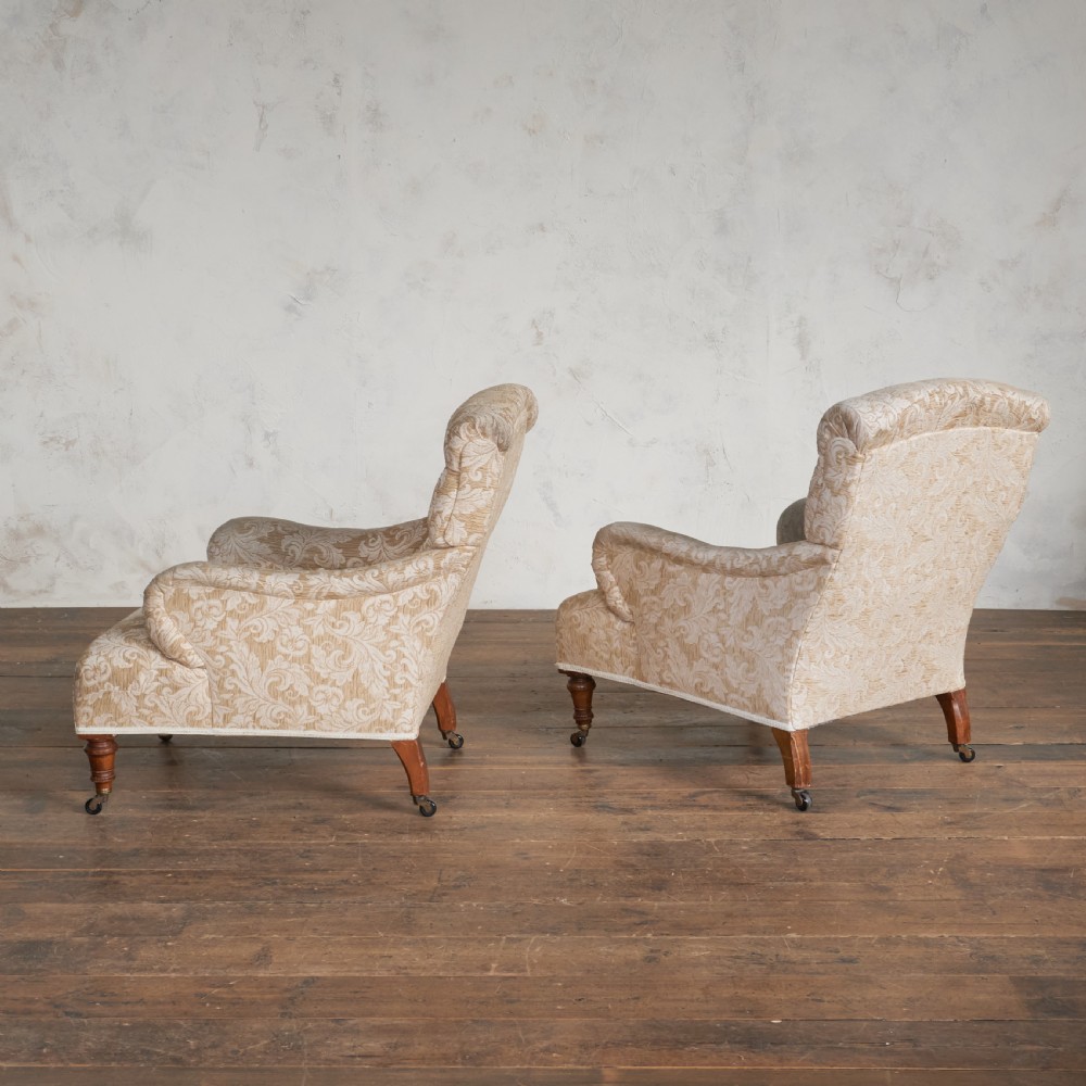 A pair of Victorian Howard style armchairs upholstered in a patterned beige fabric, featuring buttoned backs and turned wooden legs with brass castors. View III