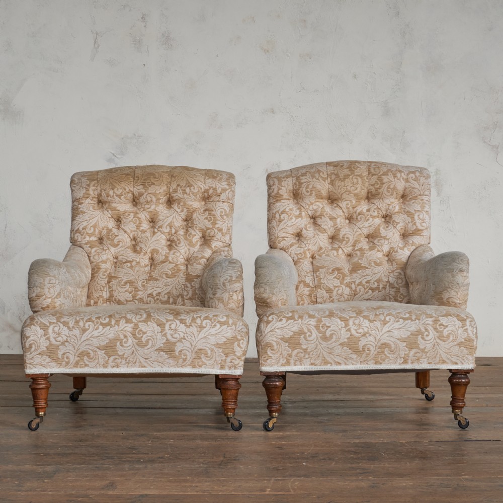 A pair of Victorian Howard style armchairs upholstered in a patterned beige fabric, featuring buttoned backs and turned wooden legs with brass castors. View IV