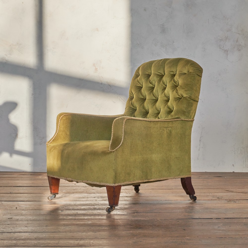 An antique armchair upholstered in green velvet with button-tufted backrest and turned wooden legs on brass castors.