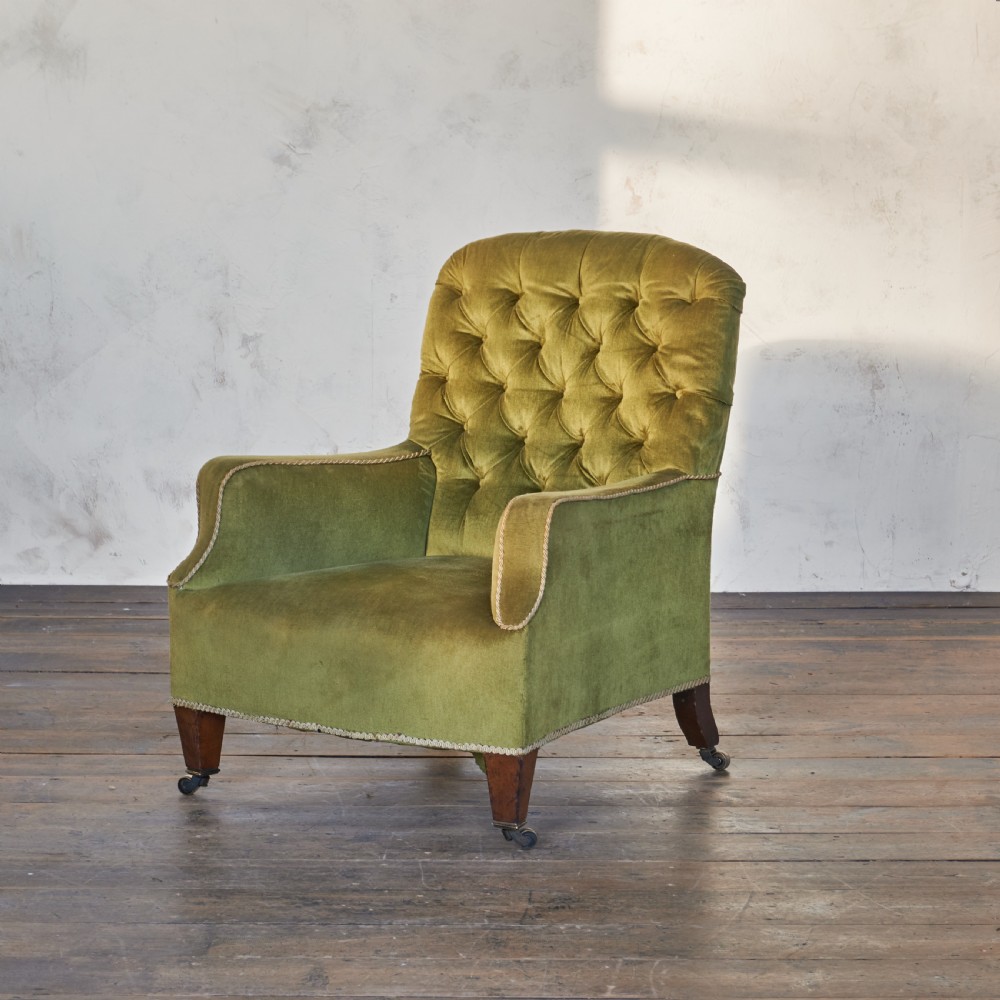 An antique armchair upholstered in green velvet with button-tufted backrest and turned wooden legs on brass castors. View III