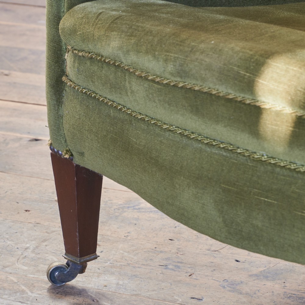 An antique green velvet wingback armchair featuring rolled arms, dark wooden legs, and brass castors. View VIII