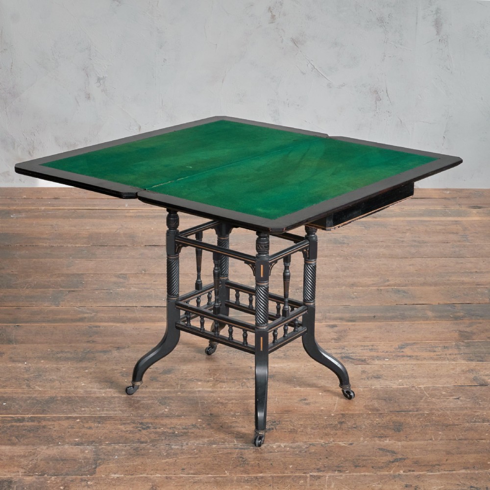 An ebonised late Victorian Aesthetic Movement card table with a rectangular fold-over top, incised gilt accents, spiral-turned legs, a lower spindle shelf, and brass castors. View III