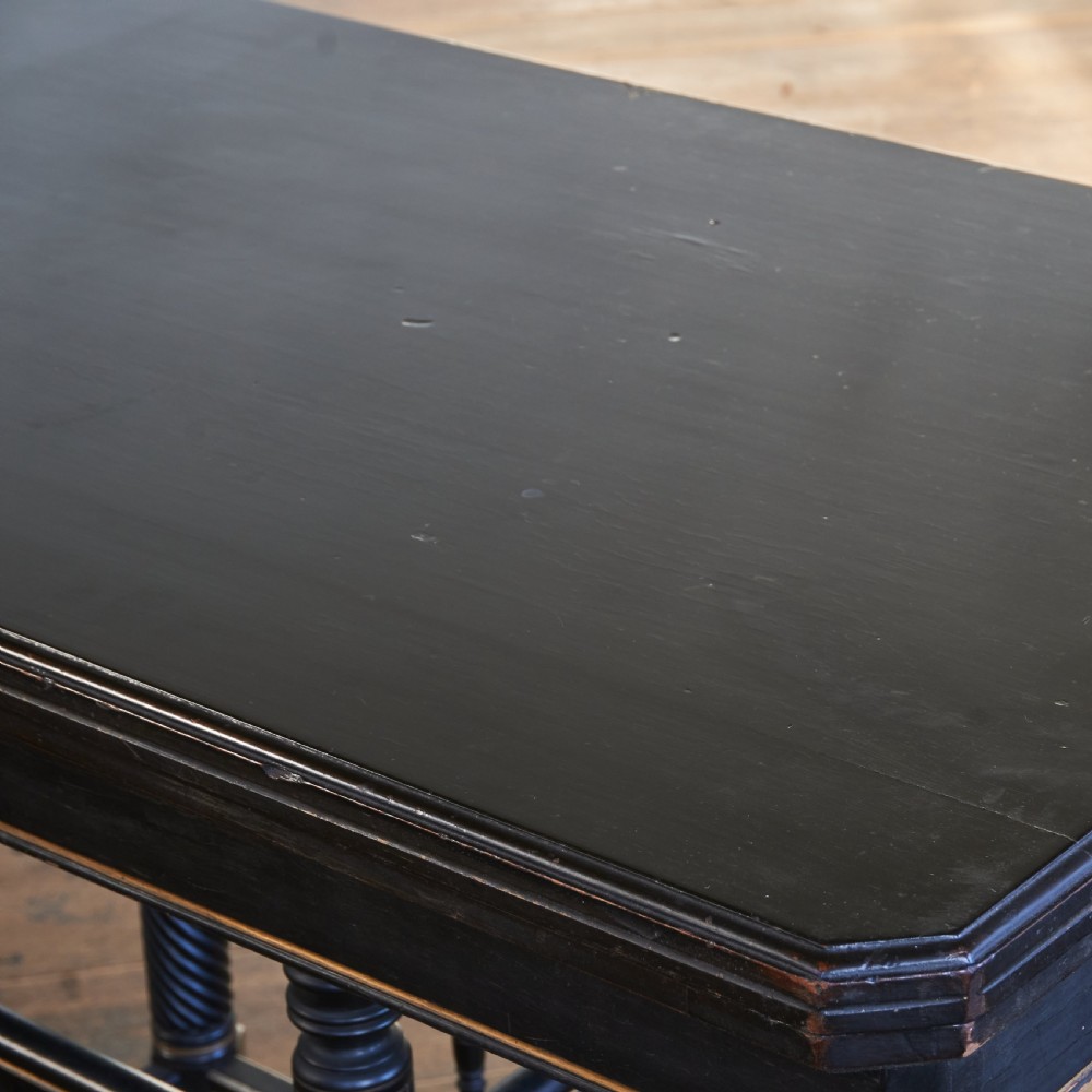 An ebonised late Victorian Aesthetic Movement card table with a rectangular fold-over top, incised gilt accents, spiral-turned legs, a lower spindle shelf, and brass castors. View VII