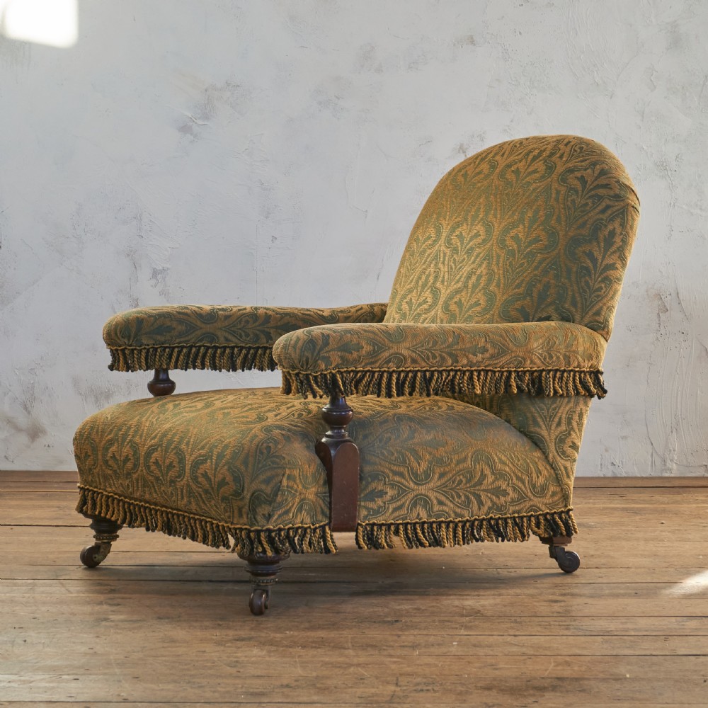 A Victorian open armchair upholstered in a patterned green and gold fabric with fringe trim on turned legs with brass castors. View VII
