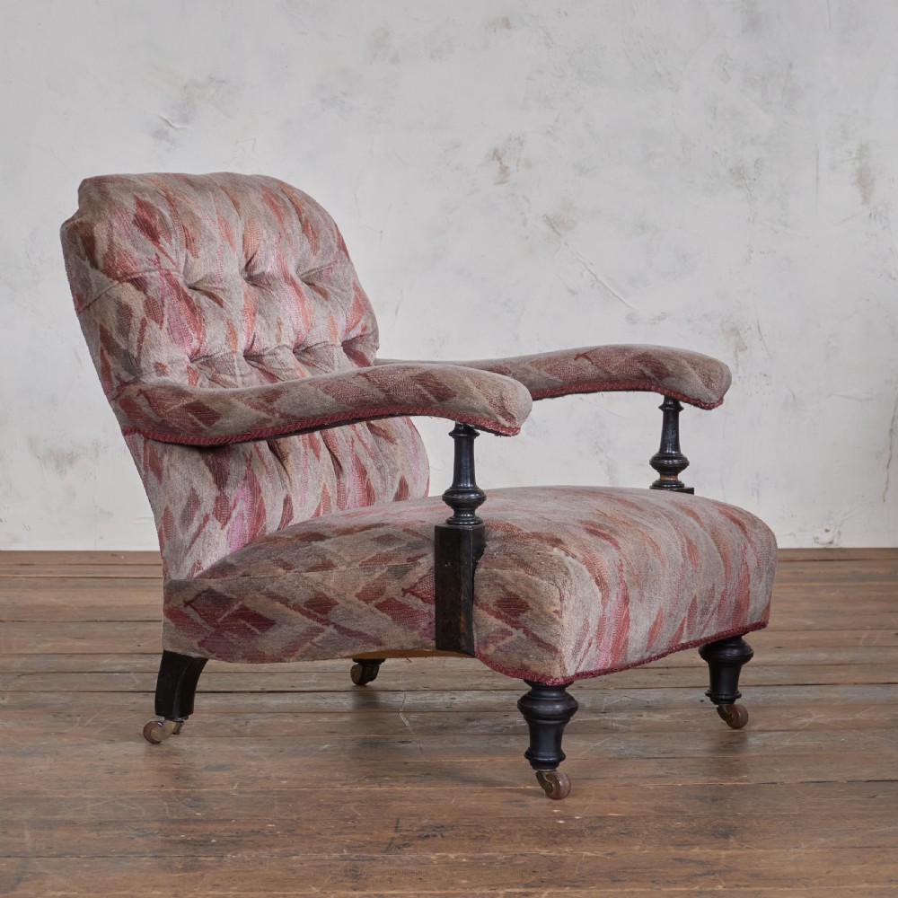 An antique upholstered open armchair featuring patterned fabric, a buttoned backrest, turned wooden legs, and brass castors.