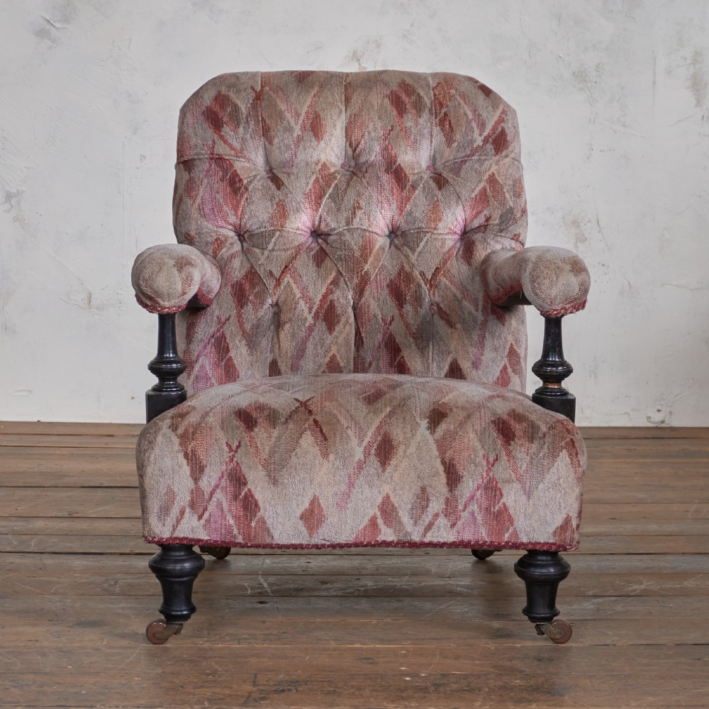 An antique upholstered open armchair featuring patterned fabric, a buttoned backrest, turned wooden legs, and brass castors. View II