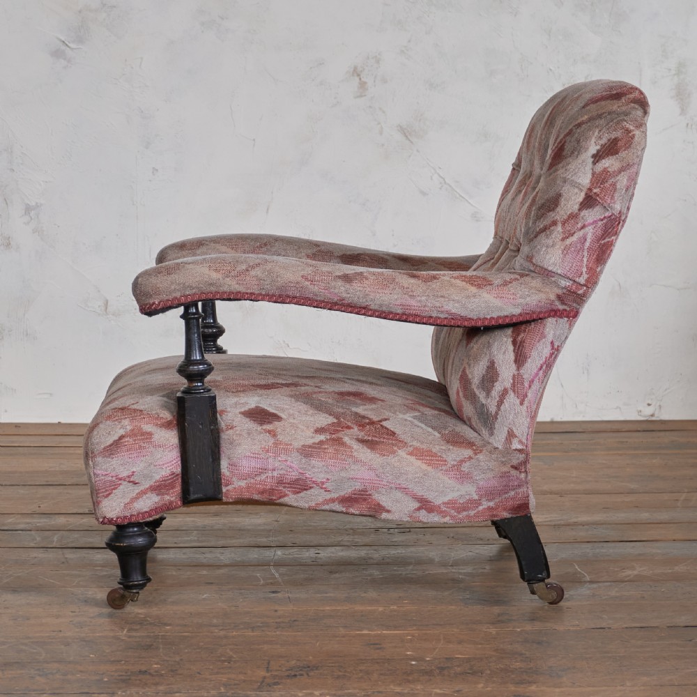 An antique upholstered open armchair featuring patterned fabric, a buttoned backrest, turned wooden legs, and brass castors. View IV