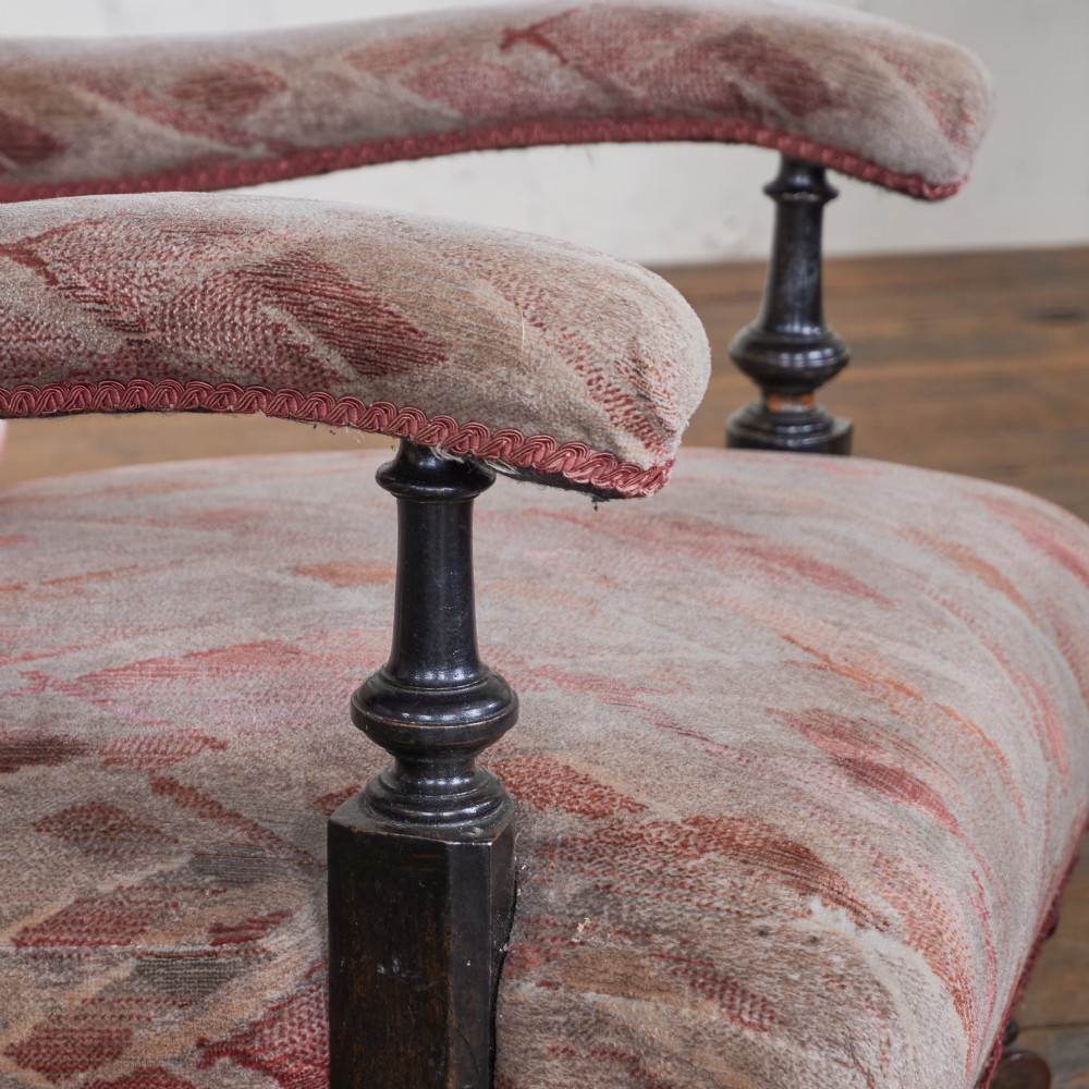 An antique upholstered open armchair featuring patterned fabric, a buttoned backrest, turned wooden legs, and brass castors. View VI