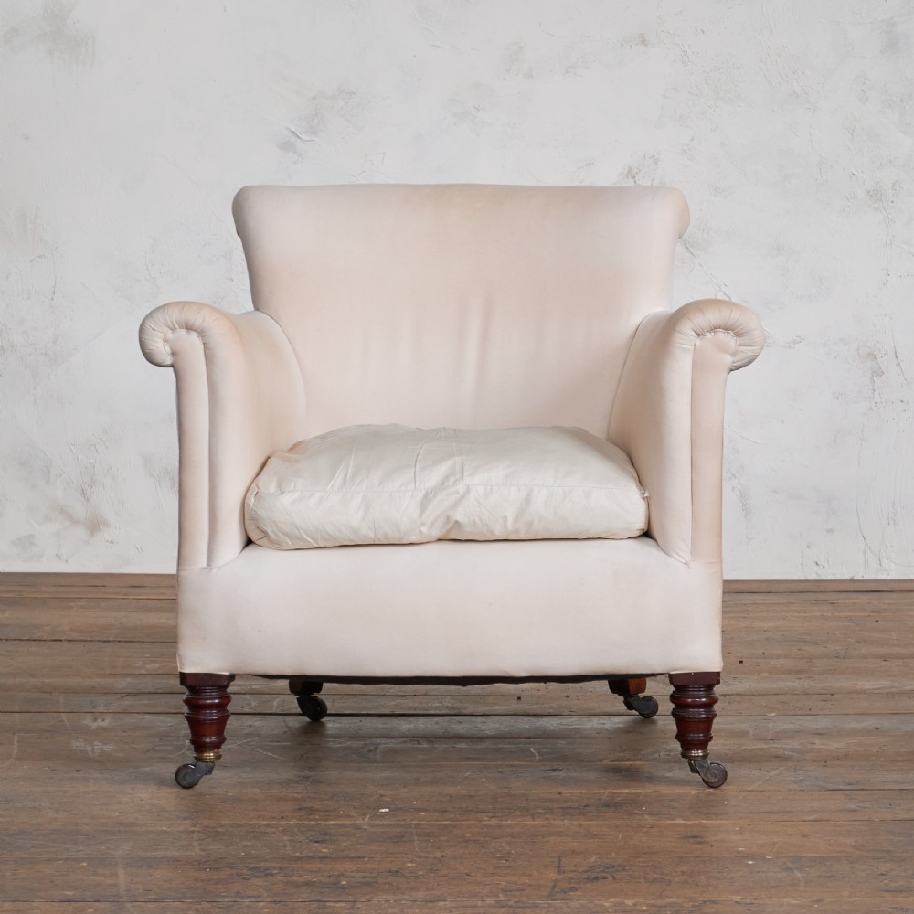 An antique cream calico upholstered tub chair featuring rolled arms, a loose seat cushion, and turned mahogany legs on brass castors.