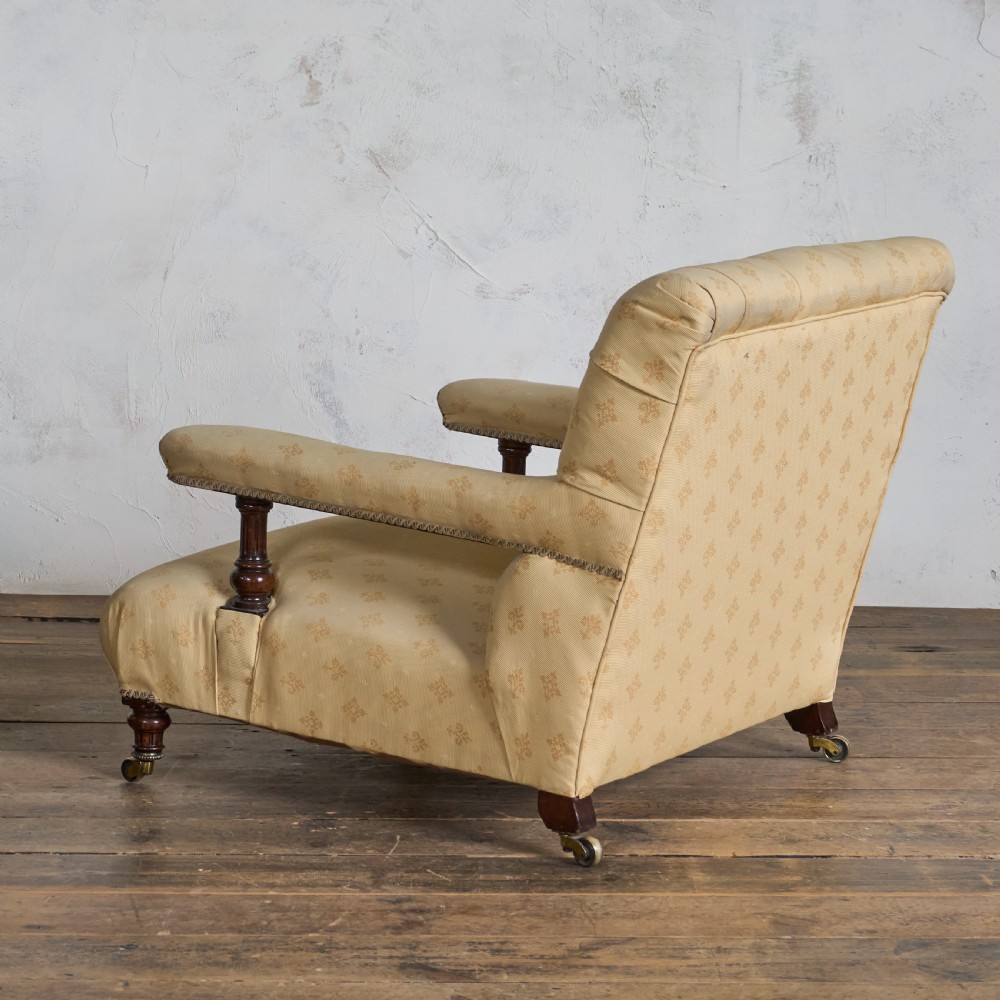 A Victorian open armchair upholstered in gold patterned fabric with a deep buttoned backrest, padded open arms on turned wood supports, and turned wooden legs fitted with brass castors. View III