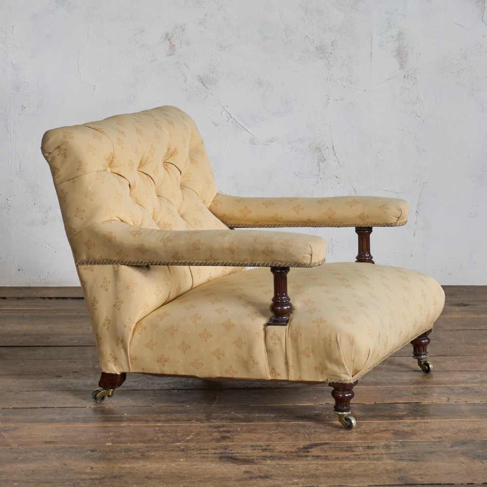 A Victorian open armchair upholstered in gold patterned fabric with a deep buttoned backrest, padded open arms on turned wood supports, and turned wooden legs fitted with brass castors. View V