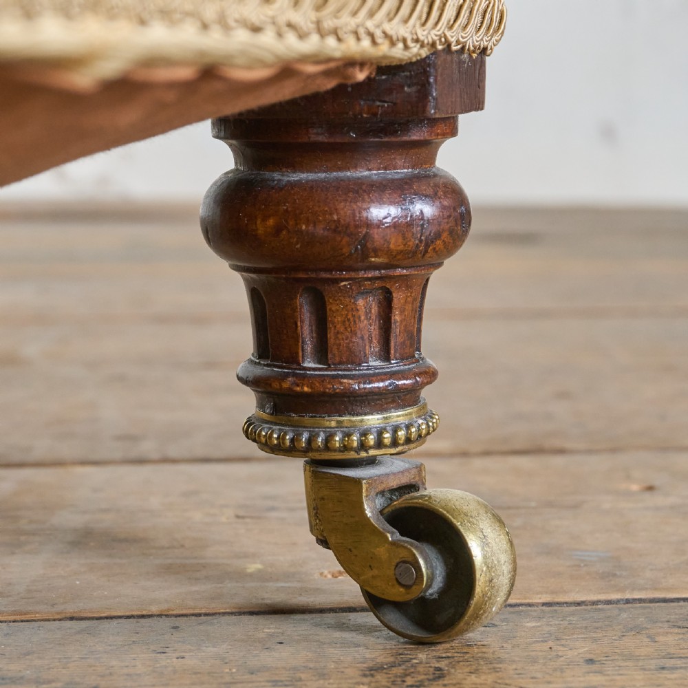 A Victorian open armchair upholstered in gold patterned fabric with a deep buttoned backrest, padded open arms on turned wood supports, and turned wooden legs fitted with brass castors. View VI