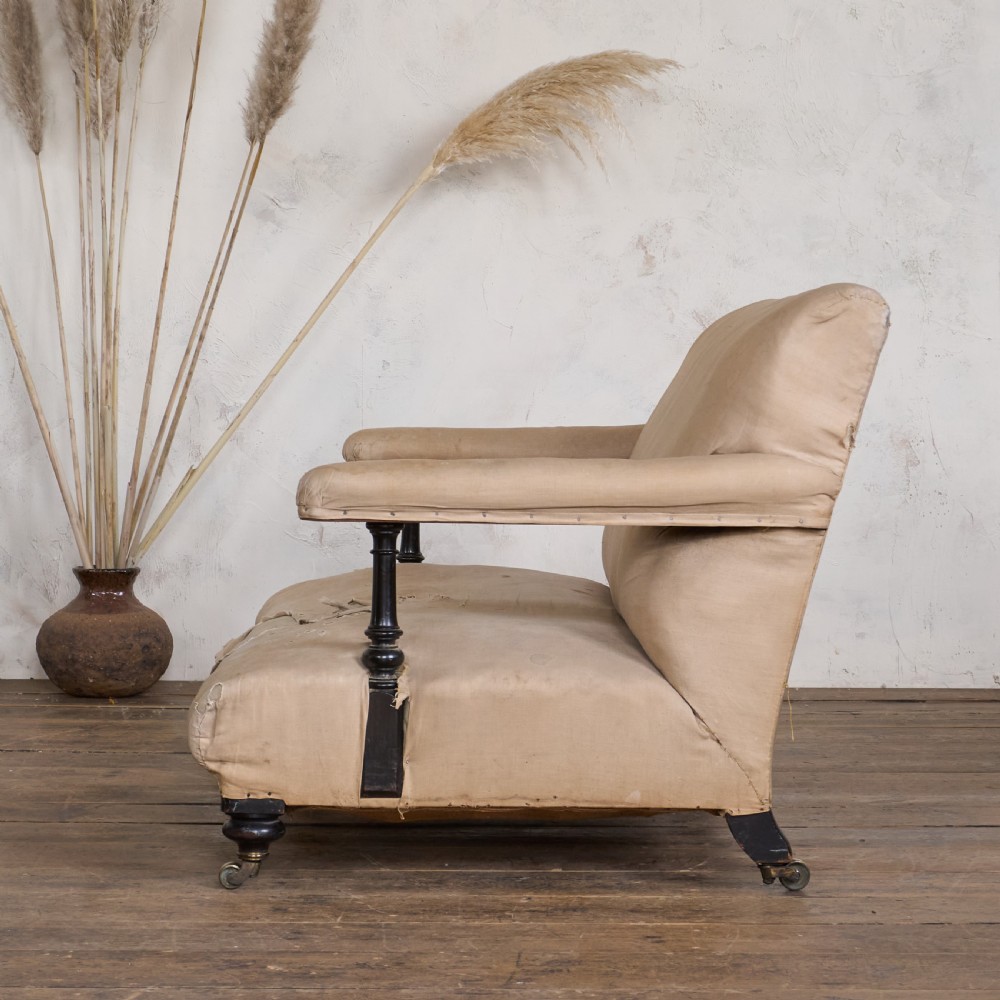 An antique two-seater open arm sofa with beige upholstery, dark turned wood legs, and brass castors. View IV