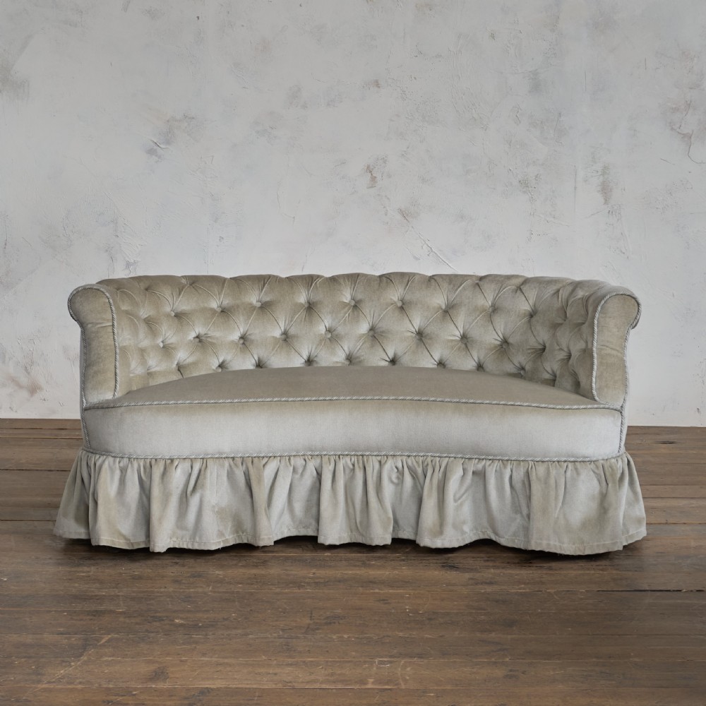 An antique Victorian kidney sofa upholstered in button-tufted pale yellow velvet with a skirted base. View II