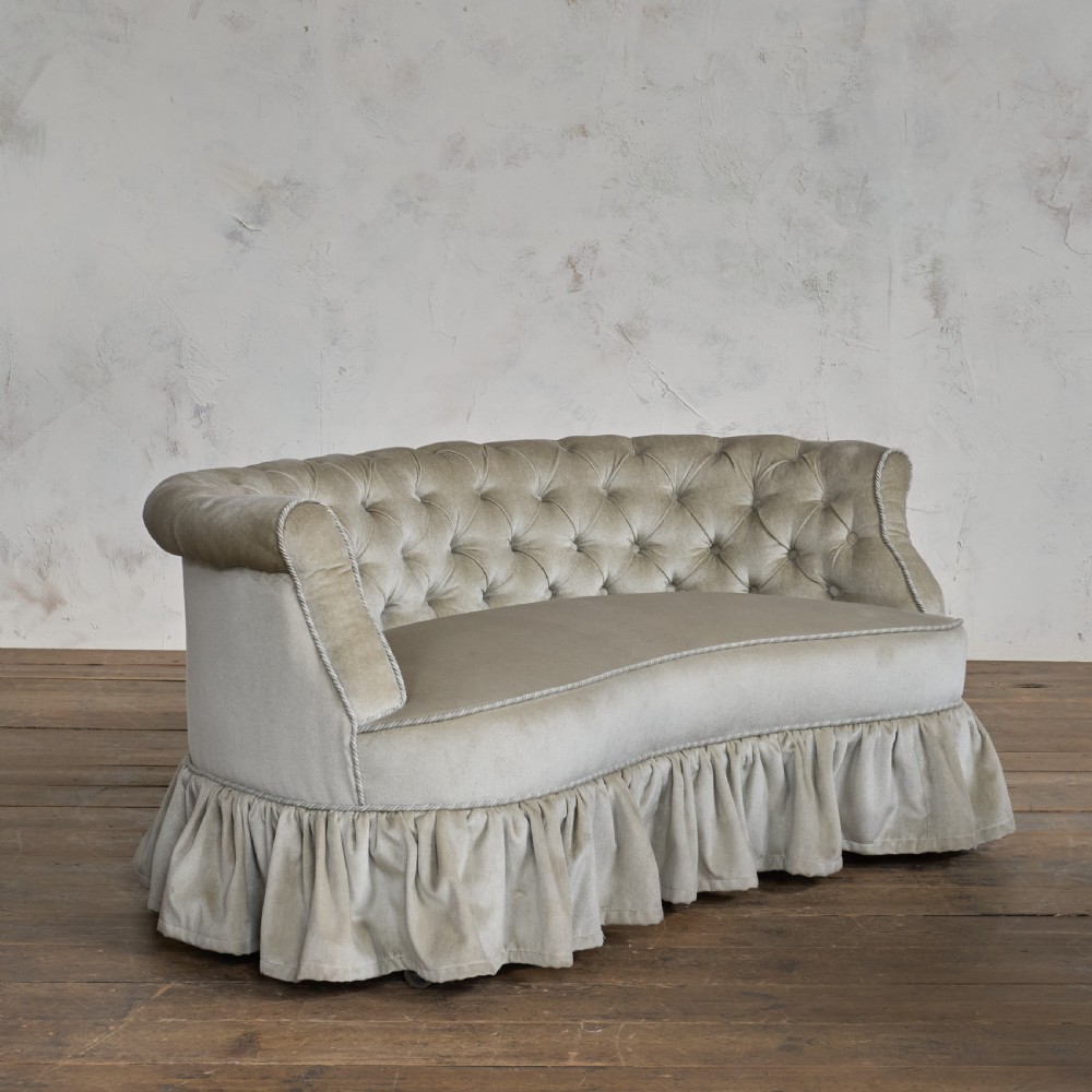 An antique Victorian kidney sofa upholstered in button-tufted pale yellow velvet with a skirted base. View III