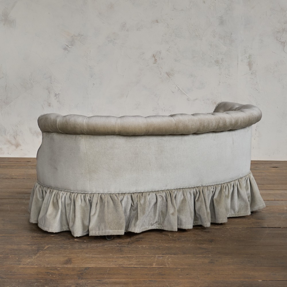 An antique Victorian kidney sofa upholstered in button-tufted pale yellow velvet with a skirted base. View V