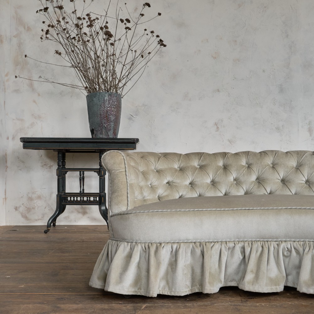 An antique Victorian kidney sofa upholstered in button-tufted pale yellow velvet with a skirted base. View X