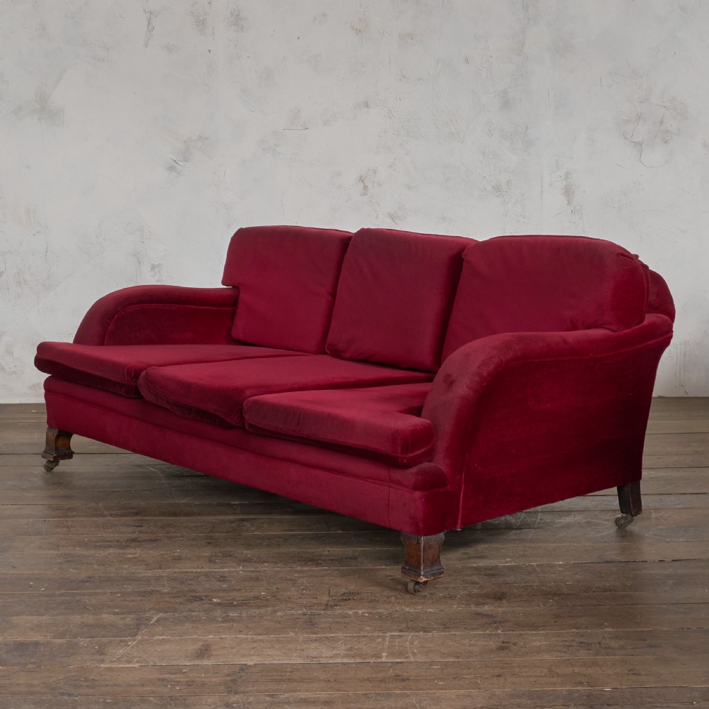 A side profile of a deep crimson velvet antique sofa featuring scroll arms and dark wood castors. View II