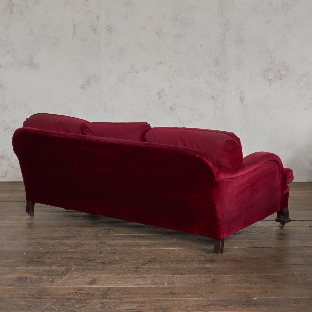 A side profile of a deep crimson velvet antique sofa featuring scroll arms and dark wood castors. View IV